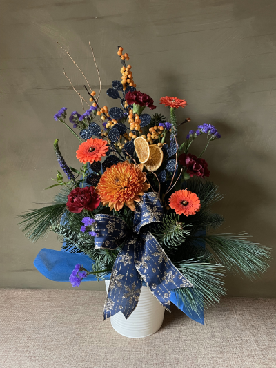 Starry Night - Presented in a stunning tin the Festive Moonlight bouquet is a stunning seasonal display of vibrant hues and rich textures. Featuring warm oranges, blues, crimsons, and shimmering accents, this arrangement exudes holiday elegance. Tied with a luxurious navy ribbon, it brings a festive glow to any space.
<br>